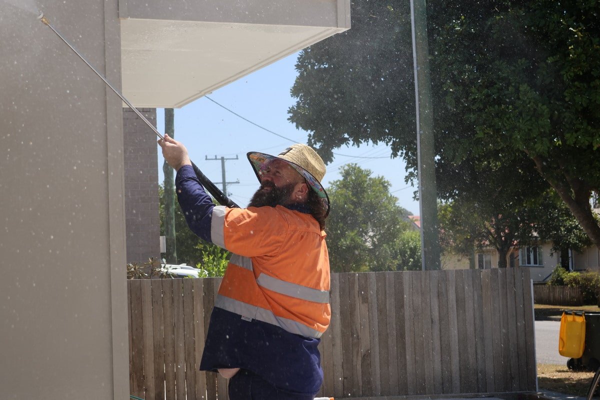 Technician pressure washing house exterior in Aspley