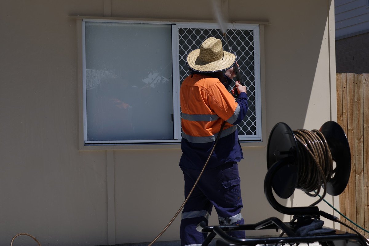 Professional cleaner pressure washing the upper part of the window of a Chermside house – Fresh Again Brisbane Northside.